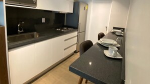 Una cocina compacta con armarios blancos, una encimera negra y un horno empotrado.