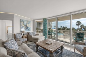 A spacious living room with a large window, a wooden coffee table, and a view of a pool and palm trees. - 3rd Floor Condo with Stunning Views and Wrap Around Balcony (Destin)