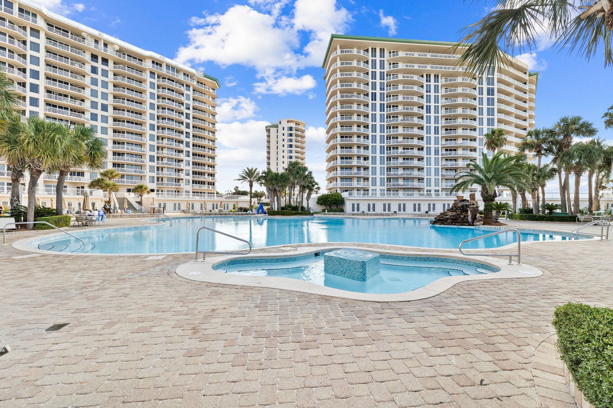 A hotel with a large pool, palm trees, and a clear blue sky.