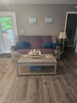 A living room with a sofa, a coffee table, and a door with a sign. - Lake House  with easy water access, limited water view, sitting on 4 acres. (Kuttawa)