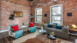 A cozy room with a brick wall, a large window, and a sign for 'Kumasi Mart & Art Gallery'. - Bright Event Perfect 4BDRM LOFT 7Min To Downtown (Detroit)