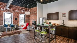 A modern kitchen with a brick wall, wooden cabinets, and a dining area with stools. - Bright Event Perfect 4BDRM LOFT 7Min To Downtown (Detroit)