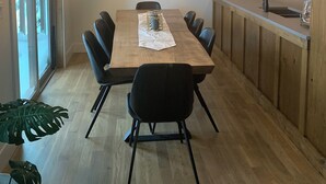 Moderni keittiö, jossa on puinen ruokapöytä, mustat tuolit ja katosta roikkuva valaisin.