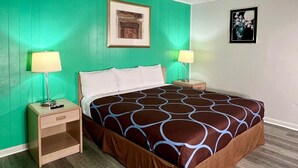 A hotel room with a bed, two bedside tables, a green wall, and a framed picture above the bed. - Village Inn (Salina)