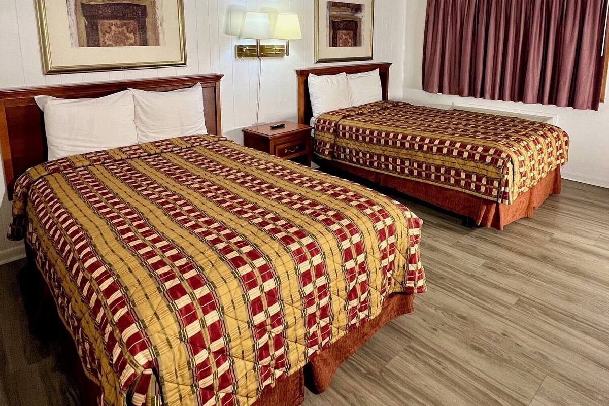 A hotel room with two beds, wooden headboards, a large window with curtains, and a ceiling vent.