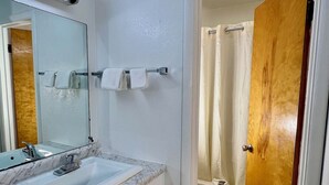 A bathroom with a marble sink, a mirror, a towel rack, a wooden door, and a shower curtain. - Village Inn (Salina)