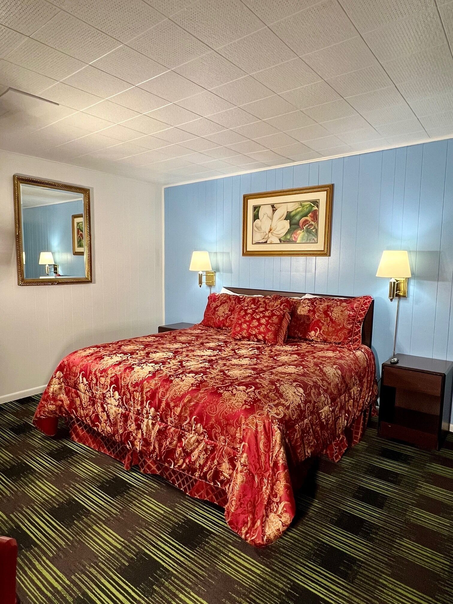 A hotel room with a large bed, two bedside lamps, a framed picture on the wall, and a mirror.