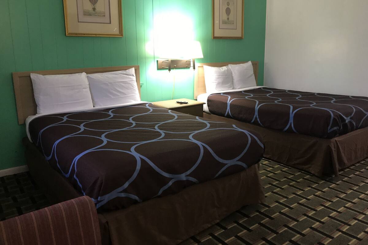 A hotel room with two beds, a nightstand, a lamp, and two framed pictures on the wall.