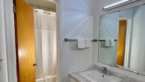 A bathroom with a white sink, mirror, and shower curtain. - Village Inn (Salina)