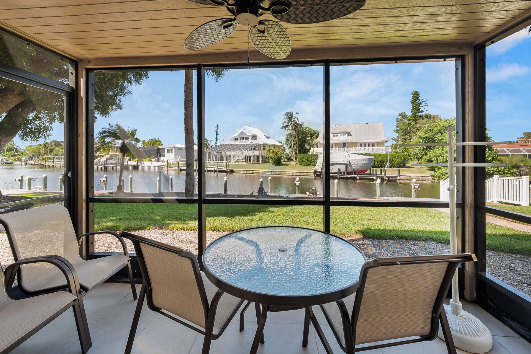 Un porche cubierto con una mesa y sillas de vidrio, con vista a una marina con barcos y casas.