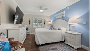 A bedroom with a bed, nightstands, a desk, a chair, a television, and a ceiling fan. - Newly Renovated Dock View 2 bed, 2 bath at Sanibel Moorings #1641 (Sanibel)
