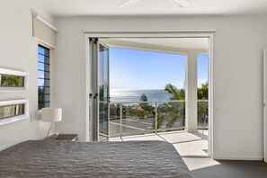 A bedroom with a bed, a nightstand, a lamp, and a sliding glass door leading to a balcony with a view of the ocean. - Relax in stylish comfort, Sunshine Beach (Sunshine Beach)