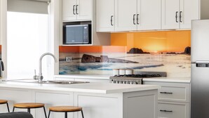 A modern kitchen with white cabinets, a built-in microwave, a gas stove, and a large window with a sunset view.