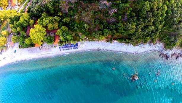 En vy över en strand från ovan, med kristallklart turkosfärgat vatten, en vit sandstrand och tät, grön vegetation.