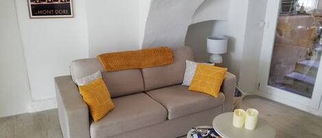 A cozy living room with a sofa, cushions, a small table with candles, and a poster on the wall.