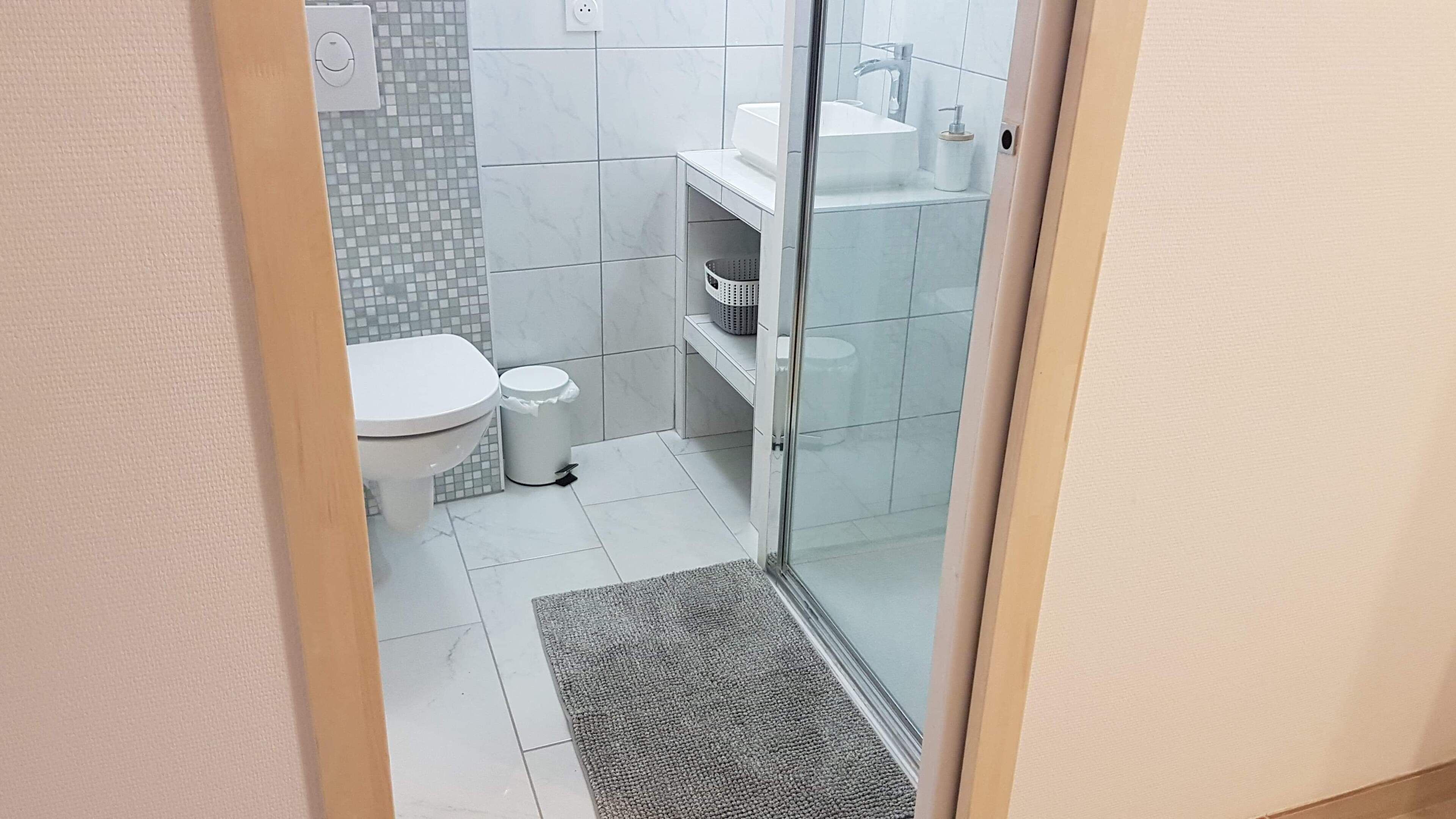 Une petite salle de bain comprenant des toilettes, une poubelle, un espace douche et un lavabo.