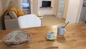 Moderni olohuone, jossa on puinen pöytä, valkoinen sohva ja seinälle asennettu televisio.