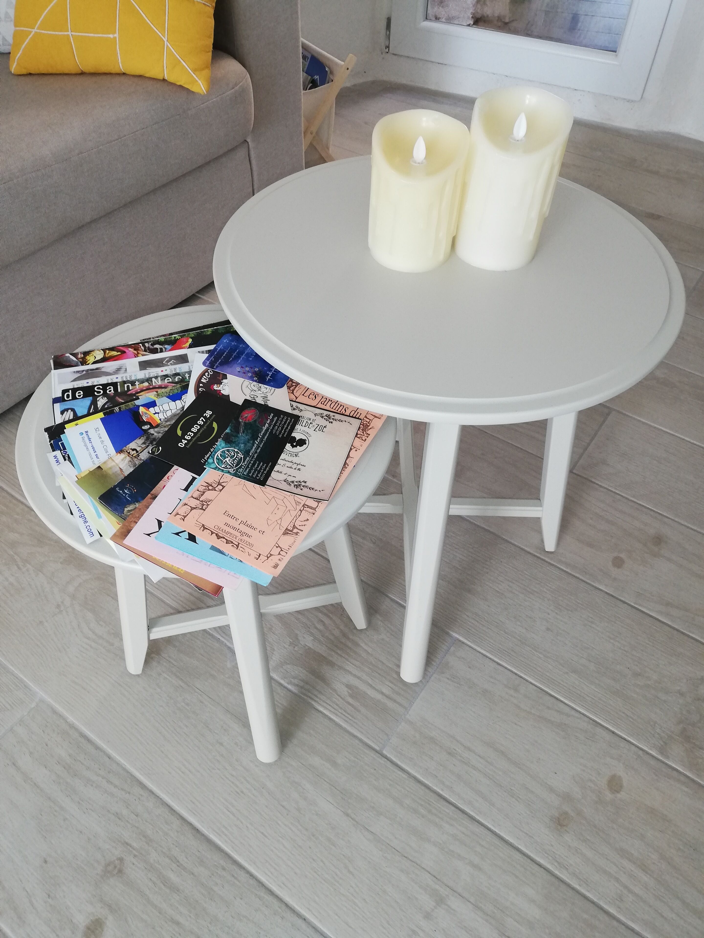 Une petite table ronde avec deux bougies et un magazine posés sur un présentoir blanc.