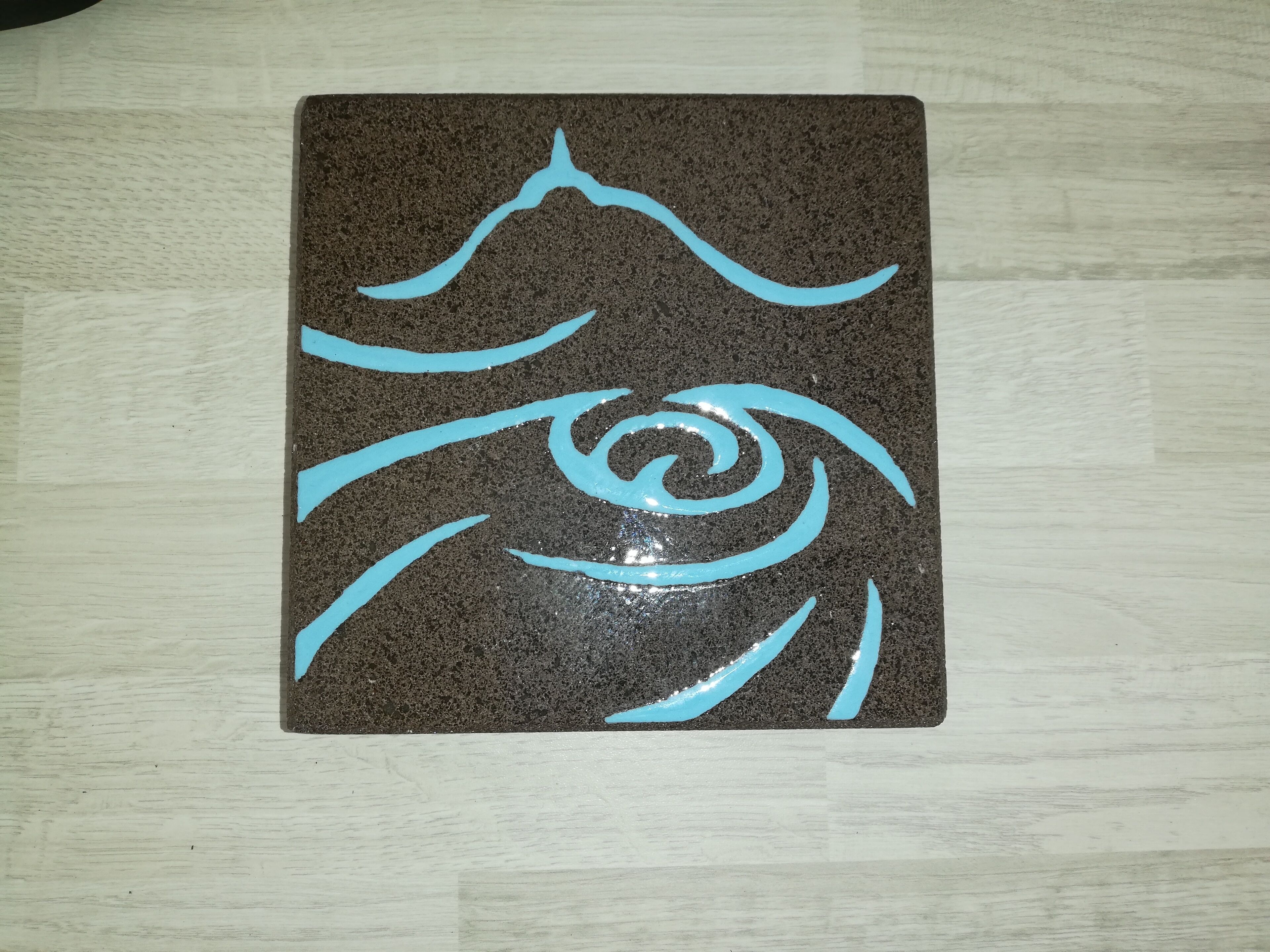 Un objeto rectangular marrón oscuro con un diseño espiral celeste sobre una superficie de madera clara.