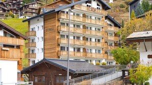 Un hôtel à plusieurs étages, doté de balcons en bois, avec un télésiège visible au loin.