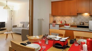 Un coin repas avec une nappe rouge, des chaises en bois et une cuisine en arrière-plan.
