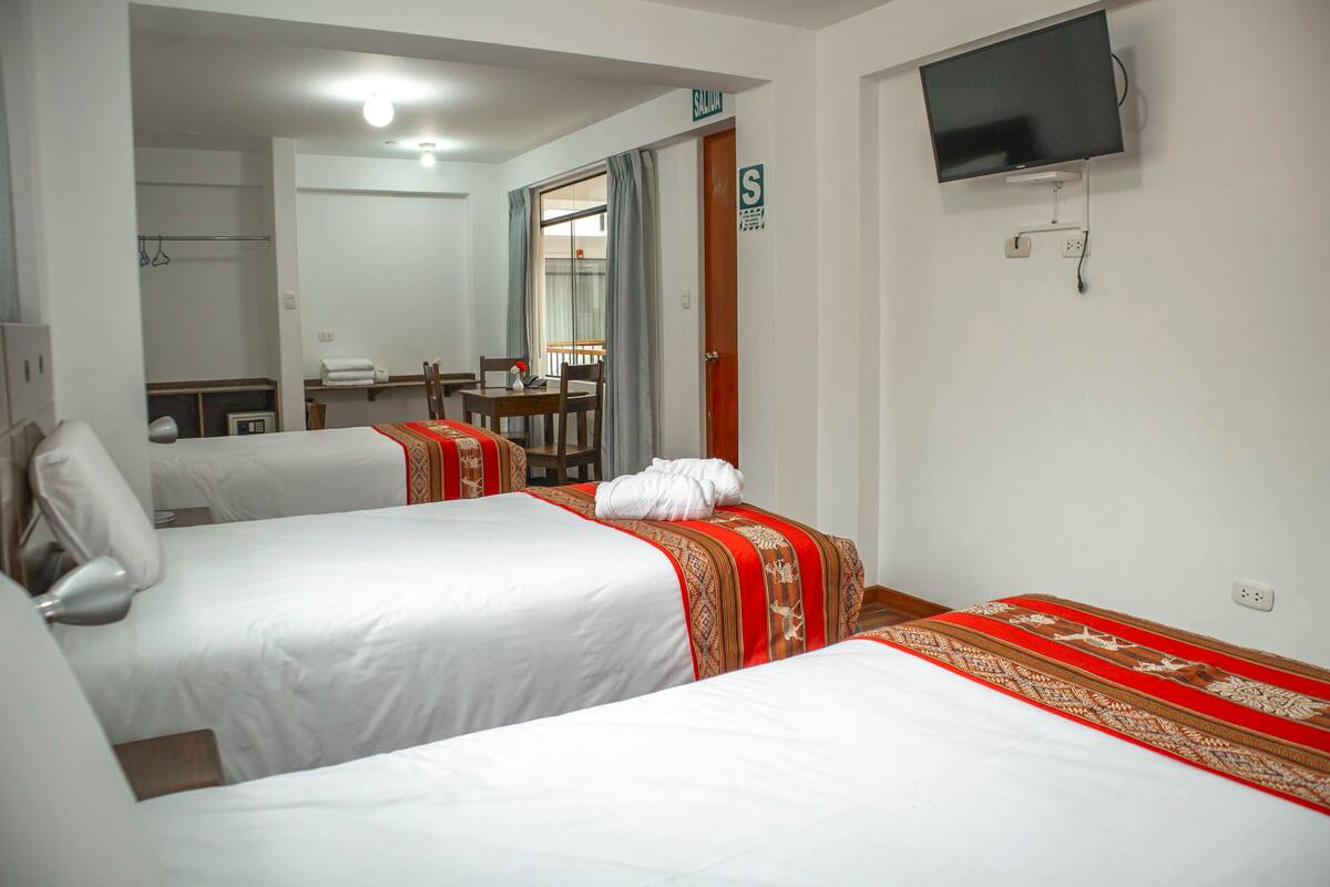 A hotel room with two beds, a television mounted on the wall, and a bathroom visible through an open door.