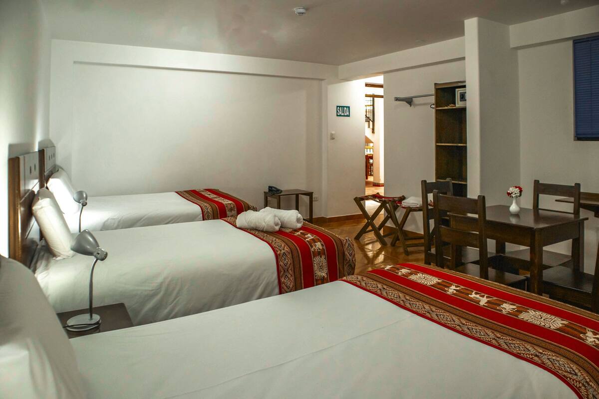 A hotel room with two beds, a desk, and a chair. There is a sign indicating the exit.