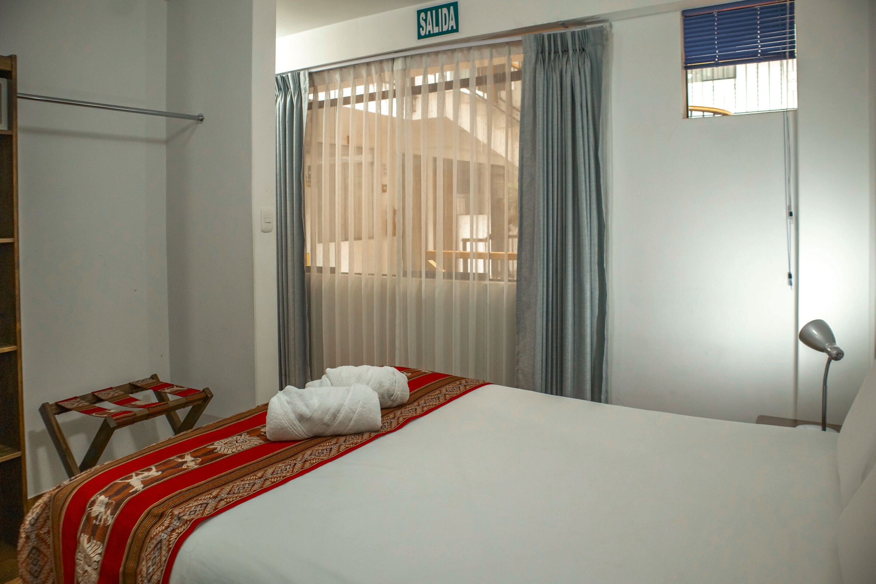 Ein Hotelzimmer mit einem Bett, einem kleinen Tisch, einem Stuhl, einer Lampe und einem Fenster mit Vorhängen.