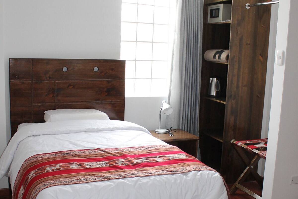 A bedroom with a wooden bed, a bedside table, a wardrobe, and a window with curtains.