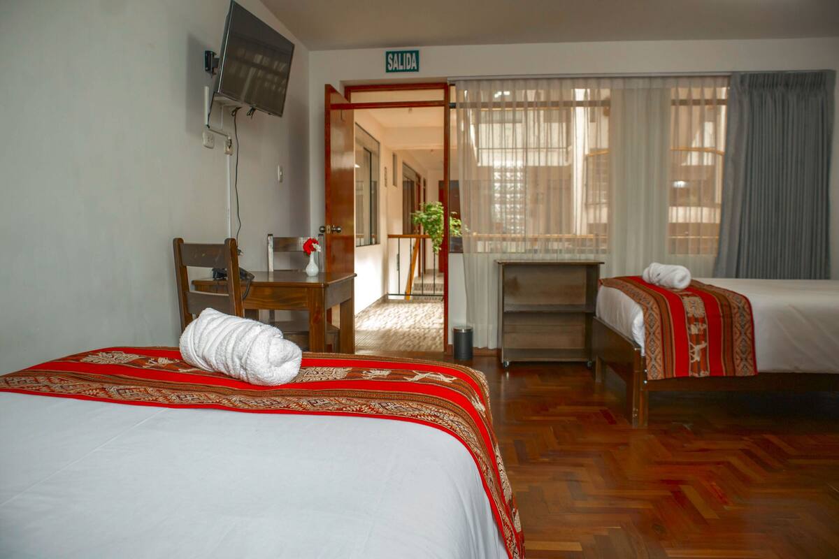 A hotel room with two beds, a desk, a chair, a TV, and a sign indicating the exit.