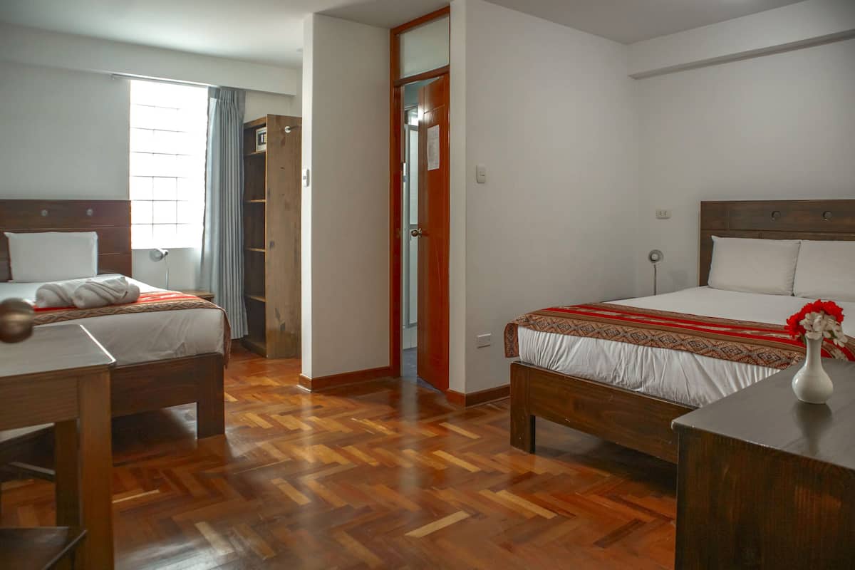 A hotel room with two beds, wooden flooring, and a wardrobe.