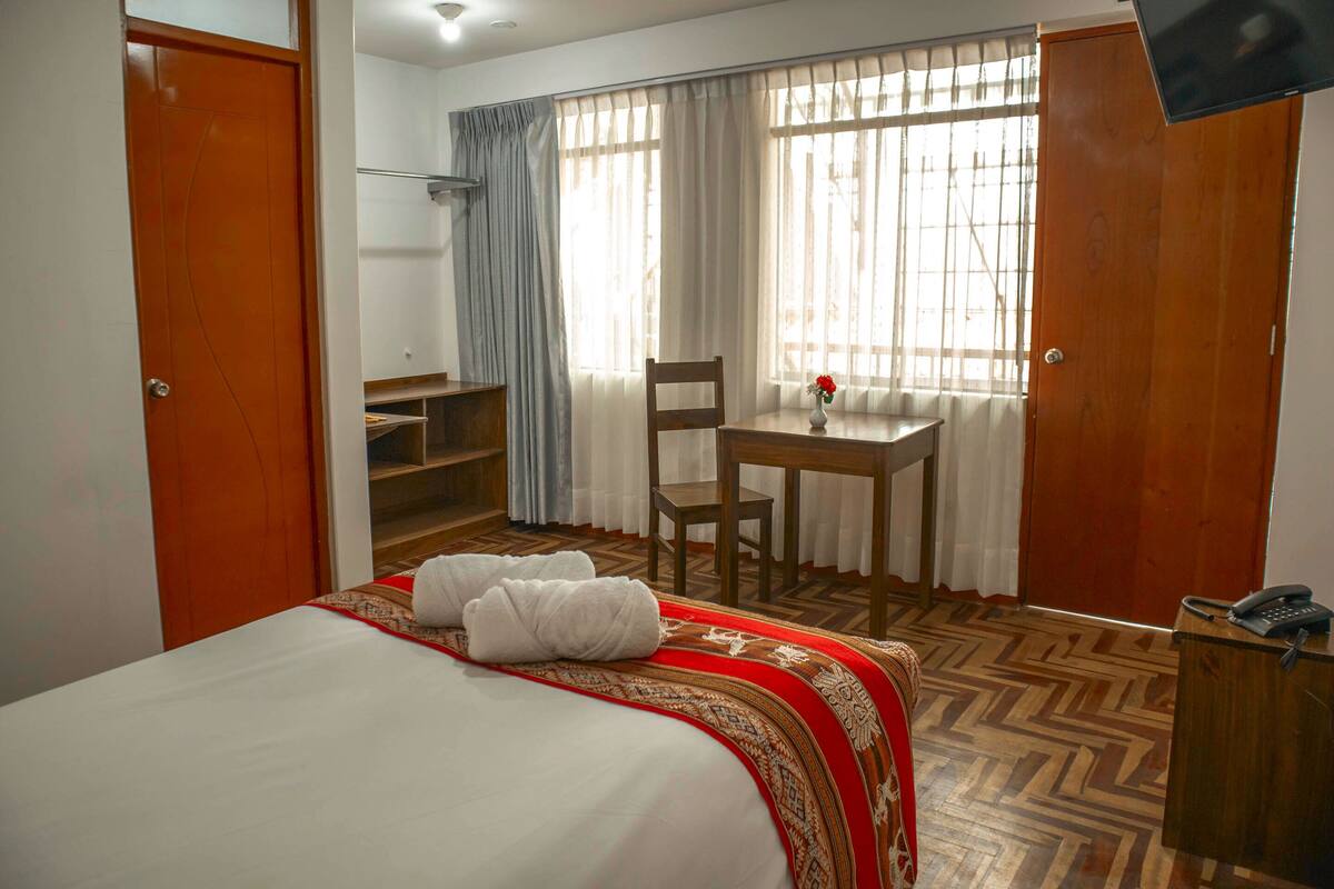 A hotel room with a bed, a desk, a chair, a wardrobe, and a window with curtains.