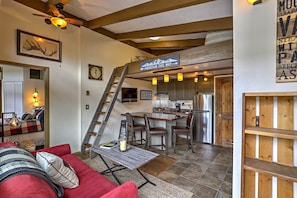 A spacious living area with a red couch, a wooden coffee table, and a staircase leading to a kitchen.