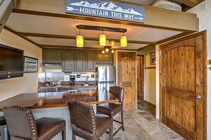 Una cocina con armarios de madera, un refrigerador de acero inoxidable, una barra con taburetes y un letrero que dice "MOUNTAIN THIS WAY".