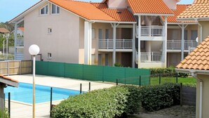 A multi-story hotel with balconies, a swimming pool, and a green fence.