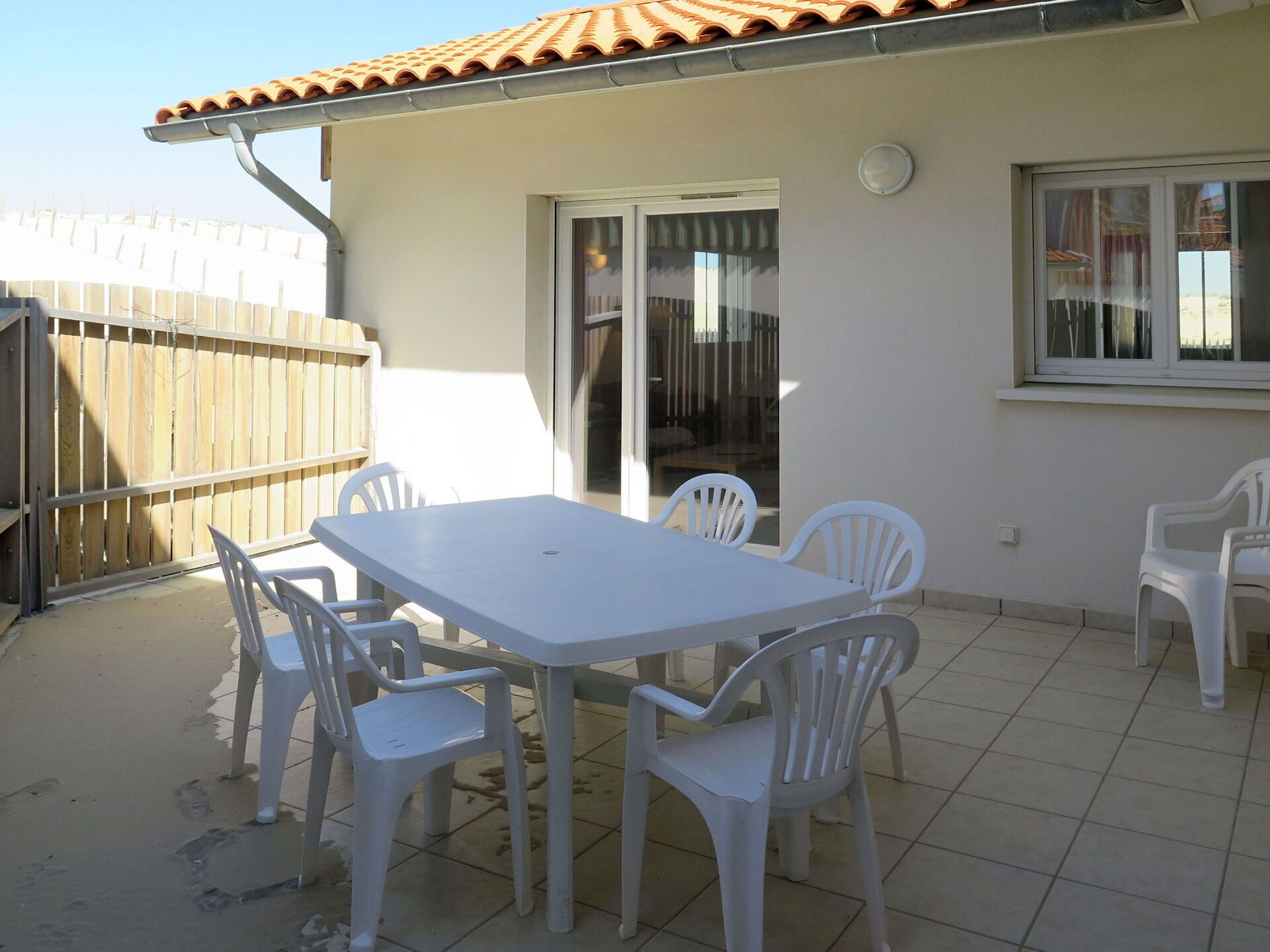 A patio with a white table and chairs, a wooden fence, and a tiled floor.