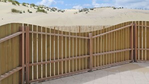 A wooden fence with a curved top, leading to a sandy beach with dunes and sparse vegetation. - Cosy apartment for 4 guests with WIFI, pool, TV, terrace and pets allowed (Biscarrosse)