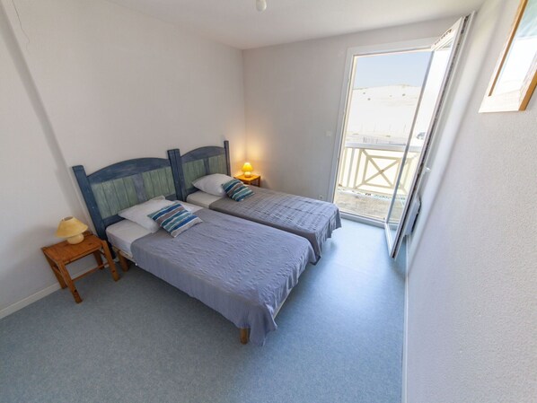 A bedroom with two beds, a nightstand, a lamp, and a window with a view of the beach.
