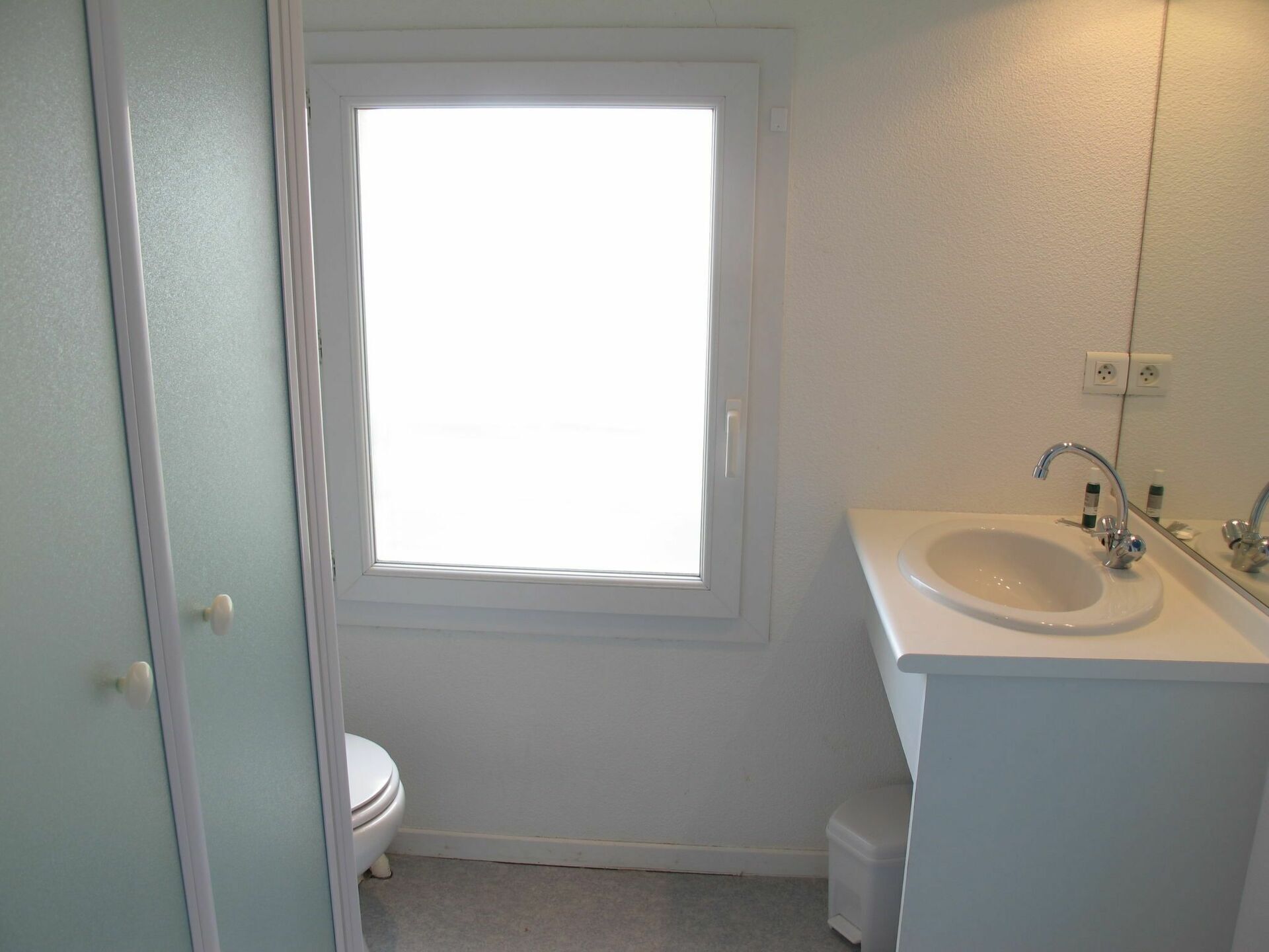 A small, clean bathroom with a toilet, sink, and window.
