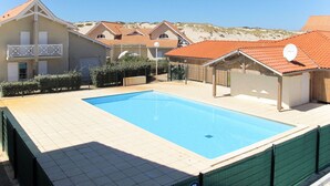 En swimmingpool omgivet af bygninger med rødløbte tage, en klar himmel og et bakket landskab i baggrunden.