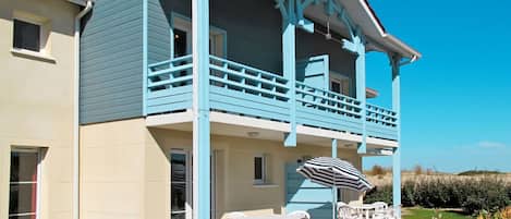 A two-story house with a balcony, a patio with outdoor furniture, and a clear blue sky.