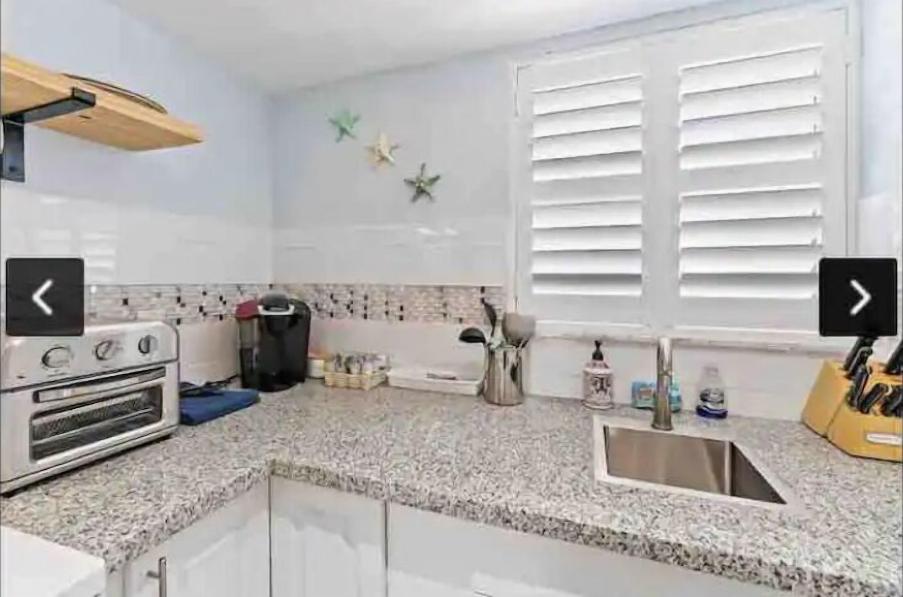 Una cocina con horno empotrado, un lavamanos y una ventana con persianas.