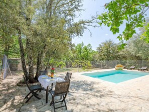 A pool area with a table and chairs, surrounded by trees and a stone patio.