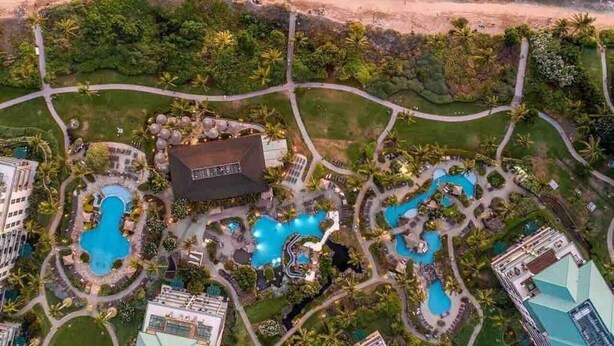 Vista aérea de un complejo turístico con varias piscinas, un edificio central y una playa.