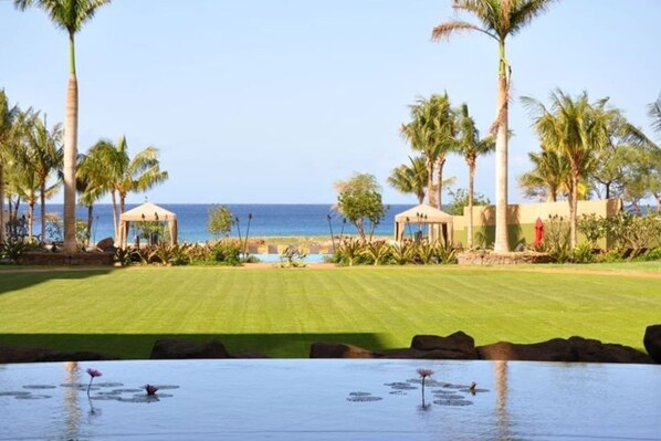 A golf course with a water feature in the foreground, palm trees, and a view of the ocean.