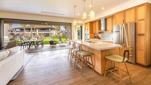 Cocina moderna con armarios de madera, una isla central con taburetes de bar y vistas a un área exterior ajardinada.
