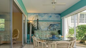 A dining area with a glass table, wicker chairs, and a mural of a beach scene on the wall.