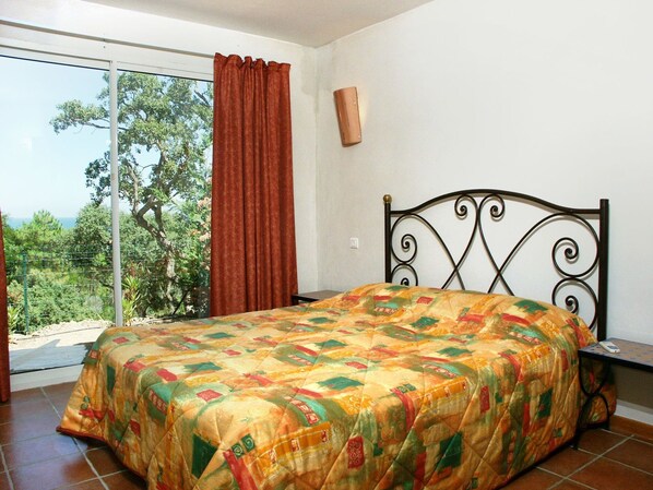 A bedroom with a bed, a window with curtains, and a view of trees.