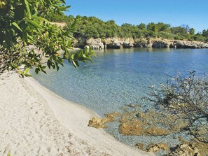 A clear coastal beach with rocky outcrops and dense greenery.