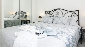 A neatly made bed with a patterned bedspread, a white towel, and a white hat on the bed.